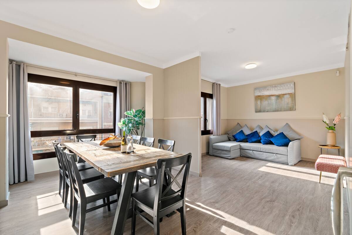 Un salón amplio con un sofá gris y una zona de comedor con mesa y sillas de madera.