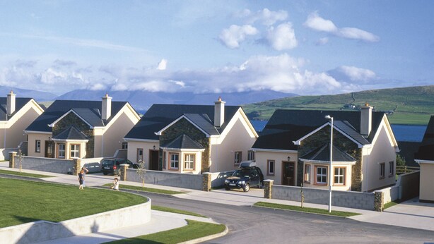 A row of modern houses with stone facades and dark roofs, set against a backdrop of hills and a clear sky. - Ard na Mara Holiday Homes (Dingle)