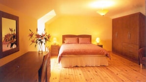 A bedroom with a bed, wooden wardrobe, bedside tables with lamps, a mirror, and a vase with flowers. - Ard na Mara Holiday Homes (Dingle)