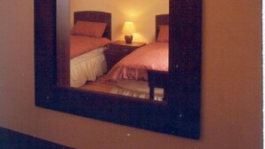 A hotel room with a large mirror reflecting two beds, a nightstand with a lamp, and a painting on the wall. - Ard na Mara Holiday Homes (Dingle)