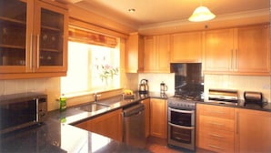 A kitchen with wooden cabinets, a stove, a microwave, and a sink. - Ard na Mara Holiday Homes (Dingle)