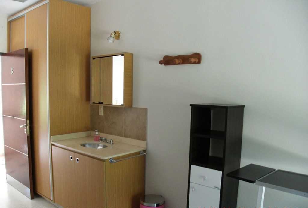 Cocina compacta con un lavamanos, un espejo y un pequeño cubo de basura.
