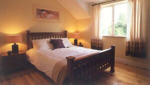 Un dormitorio con una cama de madera, dos mesitas de noche, una mesilla auxiliar, una ventana con cortinas y un cuadro en la pared.