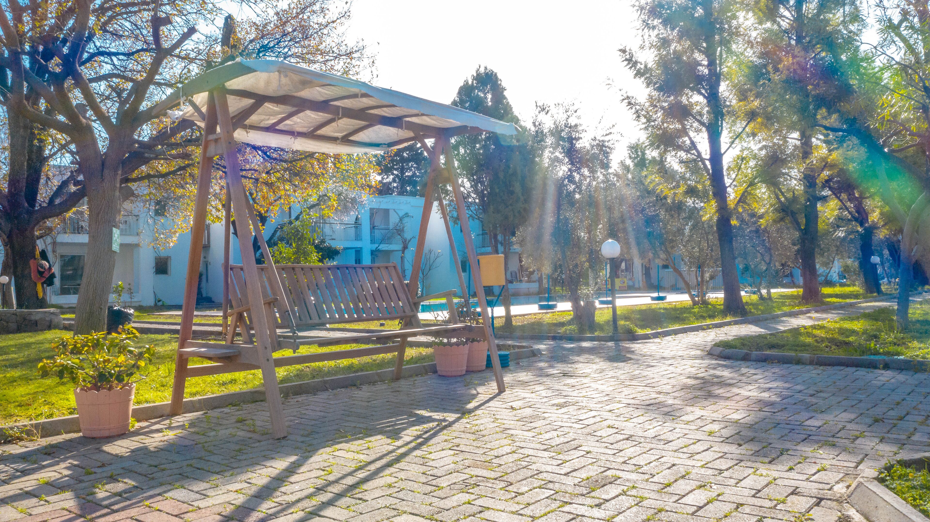 Un parque con un columpio de madera, una zona de estar cubierta y un sendero pavimentado.