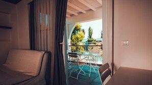 Una habitación con un sofá tapizado, un ventanal de vidrio que da a un espacio exterior con una mesa y sillas, y vistas a árboles y un edificio.