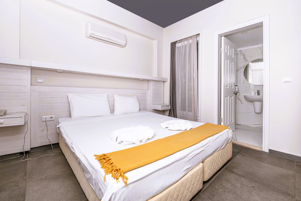 Quarto de hotel com cama, mesa de cabeceira, ar condicionado na parede e porta do banheiro.