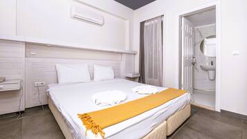 Una habitación de hotel con cama, mesita de noche, aire acondicionado de pared y puerta de baño.