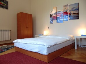A bedroom with a wooden bed, a red carpet, a white radiator, and a wall with three framed pictures.