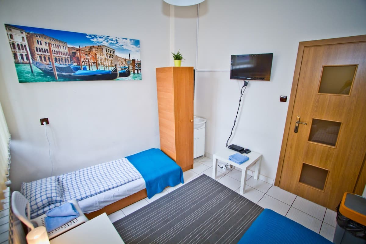 A small, clean room with two beds, a TV, a wooden wardrobe, and a painting of a canal scene.