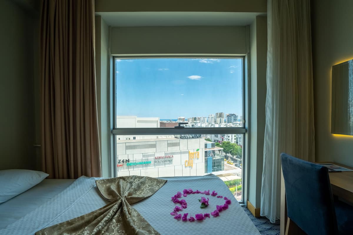 A hotel room with a large window, a bed, a desk, and a chair.