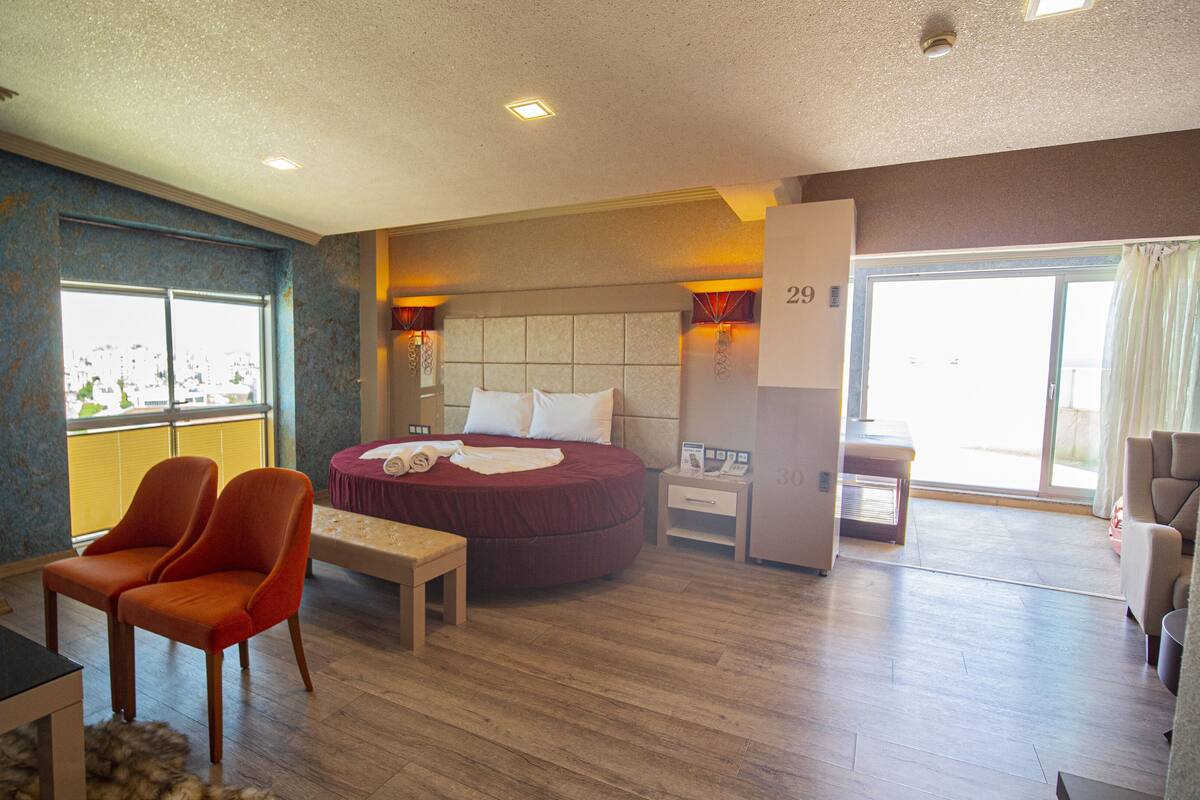 A hotel room with a bed, two chairs, a small table, a nightstand, and a window with a view.