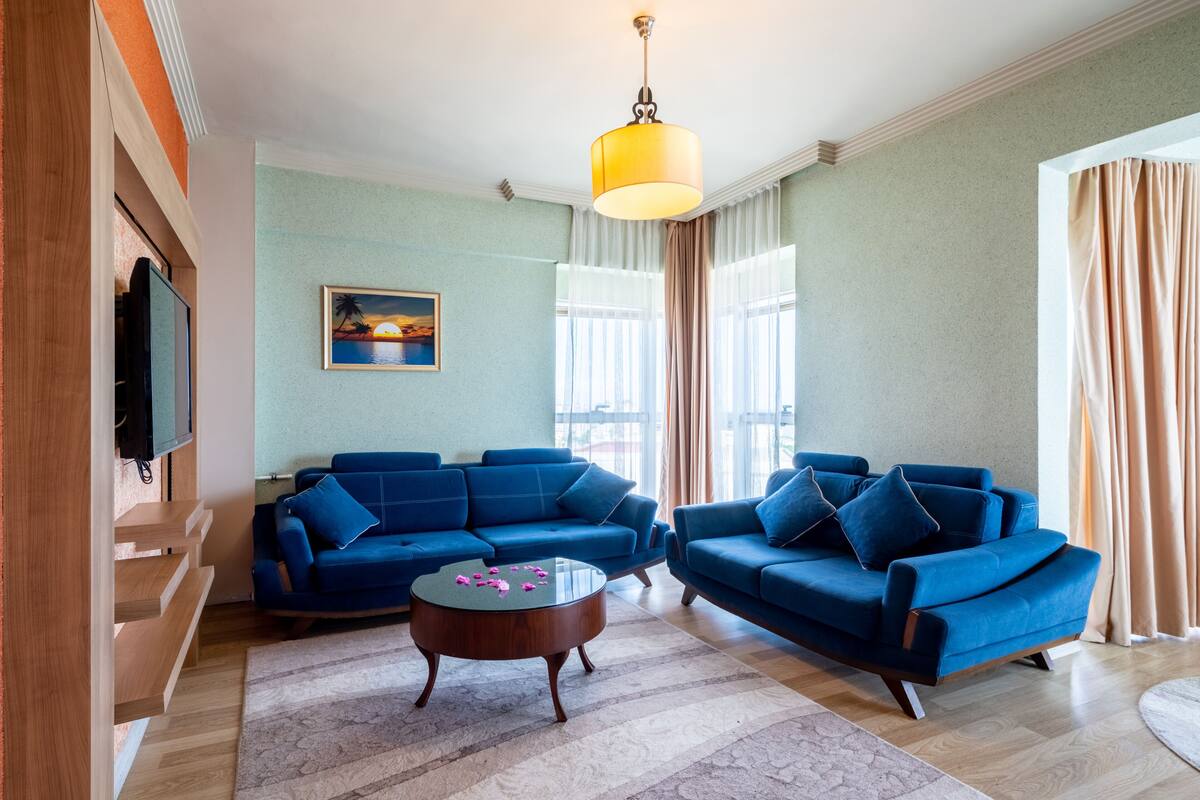A living room with two blue sofas, a coffee table, a painting on the wall, and a TV mounted on the wall.
