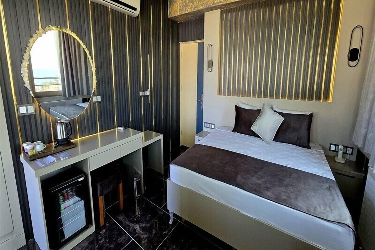 A modern hotel room with a large bed, a vanity with a mirror, a small desk, and a minibar.