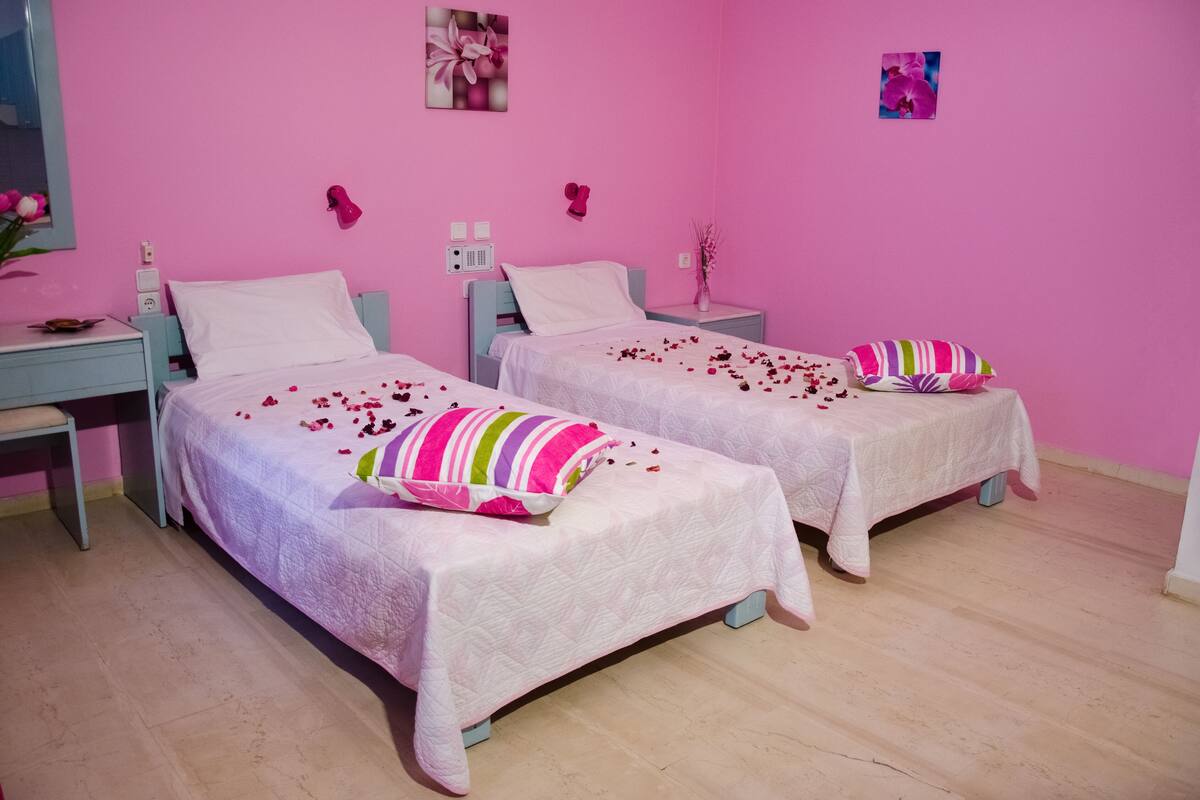 A pink-themed bedroom with two beds, each with a white quilt and colorful pillows.