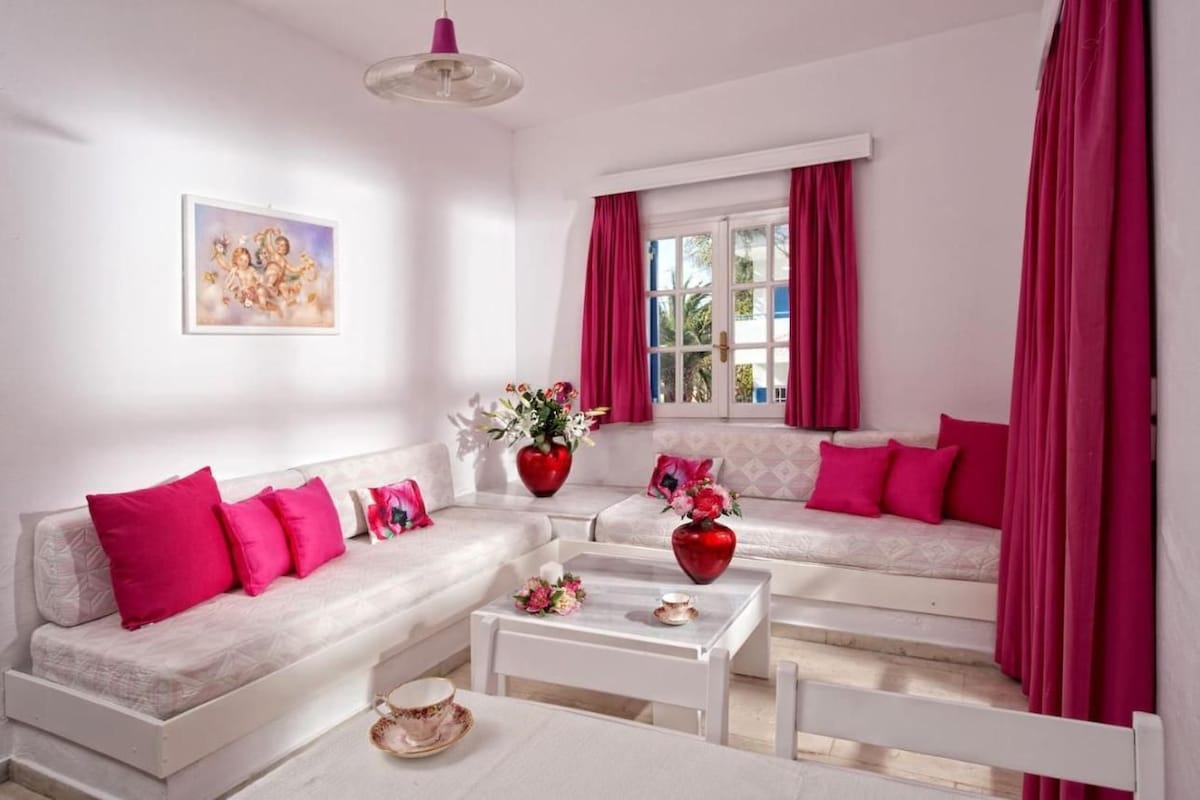 Un moderno salón con un sofá blanco, una mesa de centro y una ventana con cortinas rosas.