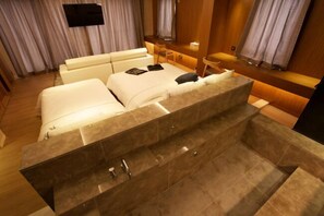 A modern hotel room with a large bed, a seating area, and a built-in bathtub. - Hotel Cullinan Jeju (Jeju City)