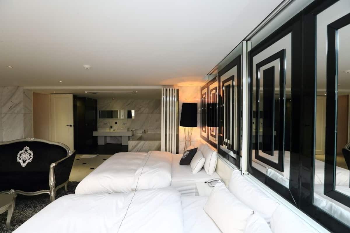 Habitación de hotel con una cama grande, un sillón negro y un baño moderno visible a través de un panel de vidrio.