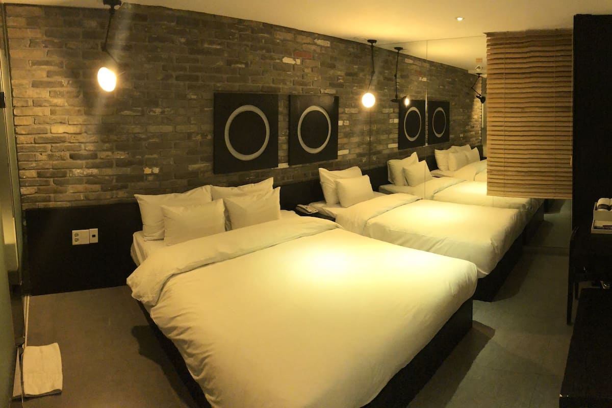 Habitación de hotel con tres camas, una pared de ladrillo y un espejo.