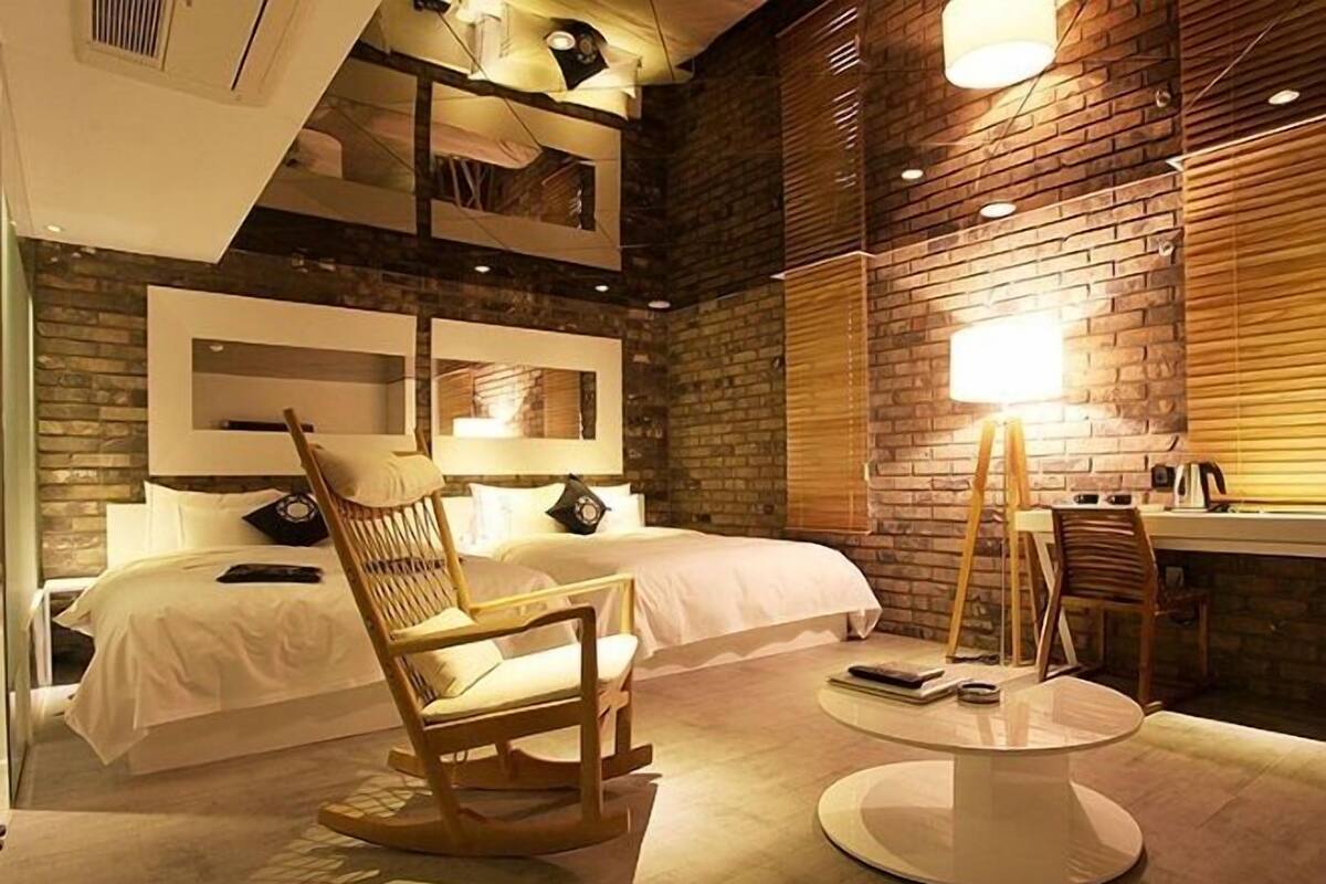 Habitación de hotel con una cama, una silla de madera, una mesa redonda y un escritorio con una lámpara.