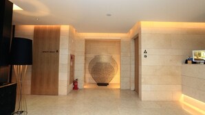 Un vestíbulo de hotel con un mostrador de recepción de madera, un jarrón decorativo grande y un extintor.