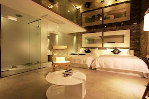 Une chambre d’hôtel moderne avec un mur en verre, un lit, une chaise et une petite table.