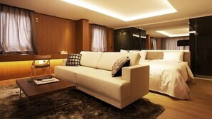 Una habitación de hotel moderna con un sofá grande, otro más pequeño, una cama y un escritorio con lámpara.