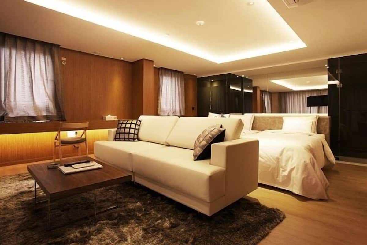 Una habitación de hotel moderna con un sofá grande, otro más pequeño, una cama y un escritorio con lámpara.