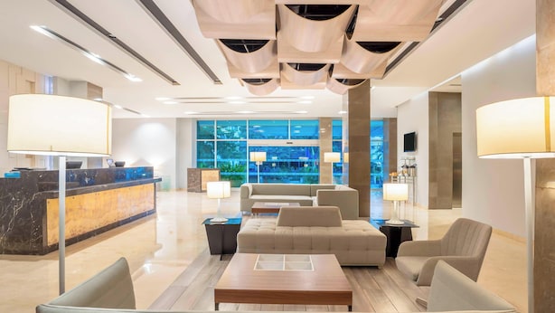 A modern lobby with a reception desk, seating area, and large windows offering a view of the city. - Four Points By Sheraton Barranquilla (Barranquilla)