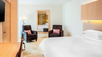 Une chambre d’hôtel avec un grand lit, deux fauteuils, un téléviseur à écran plat et un miroir.