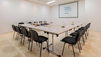 A conference room with a long table, black chairs, and a projector screen displaying "FOUR POINTS BY SHERATON".