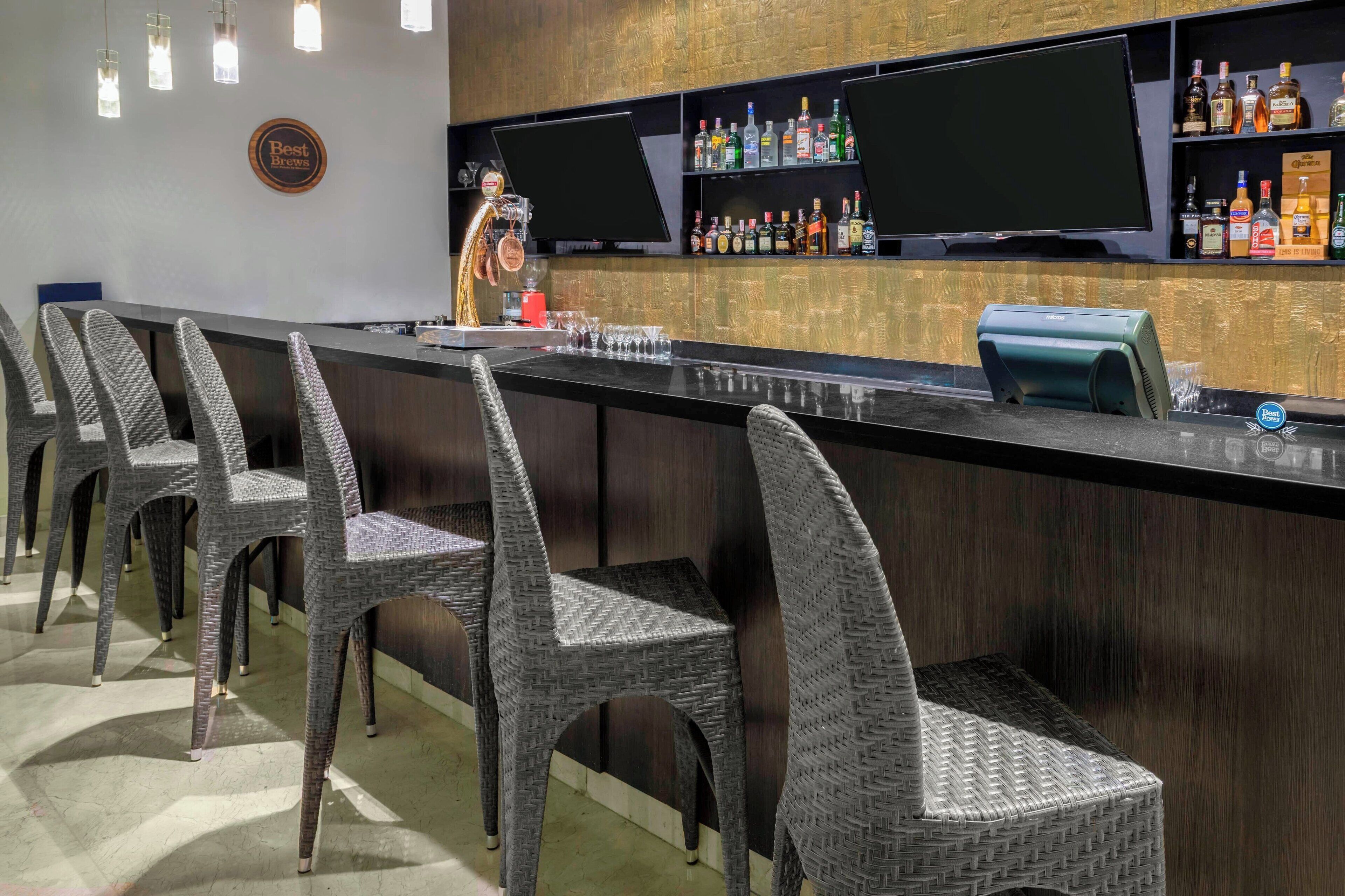 Zona de bar con sillas de mimbre, una barra con caja registradora y estantes con botellas de licor.