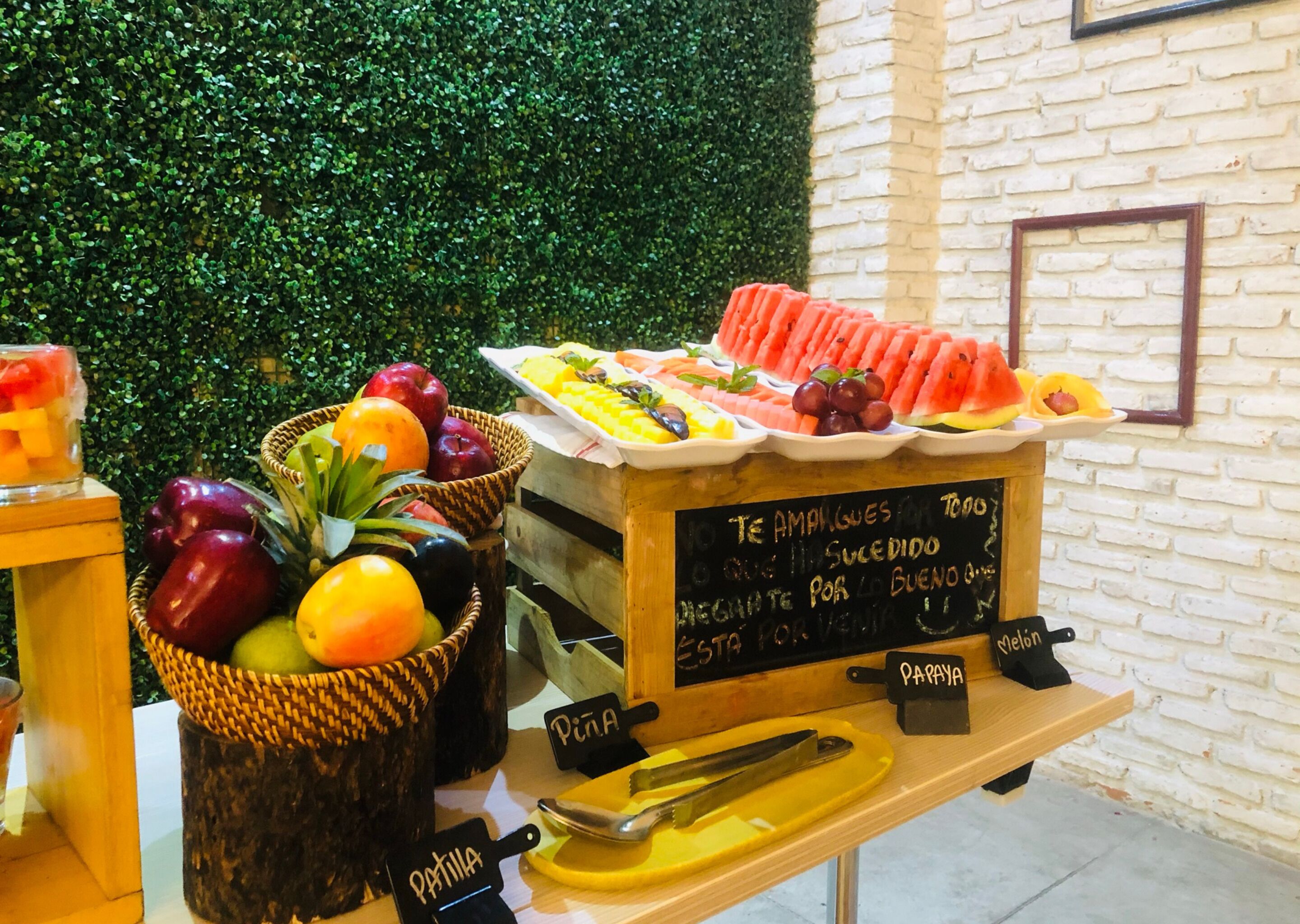 A fruit display with baskets labeled "Papaya" and "Pita," and a chalkboard sign with text in Spanish.