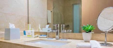 Un baño moderno con lavabo de mármol, espejo, planta y artículos de aseo.