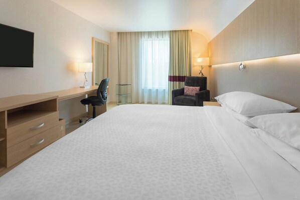 A hotel room with a large bed, a desk with a chair, a TV mounted on the wall, and a window with curtains. - Four Points By Sheraton Barranquilla (Barranquilla)