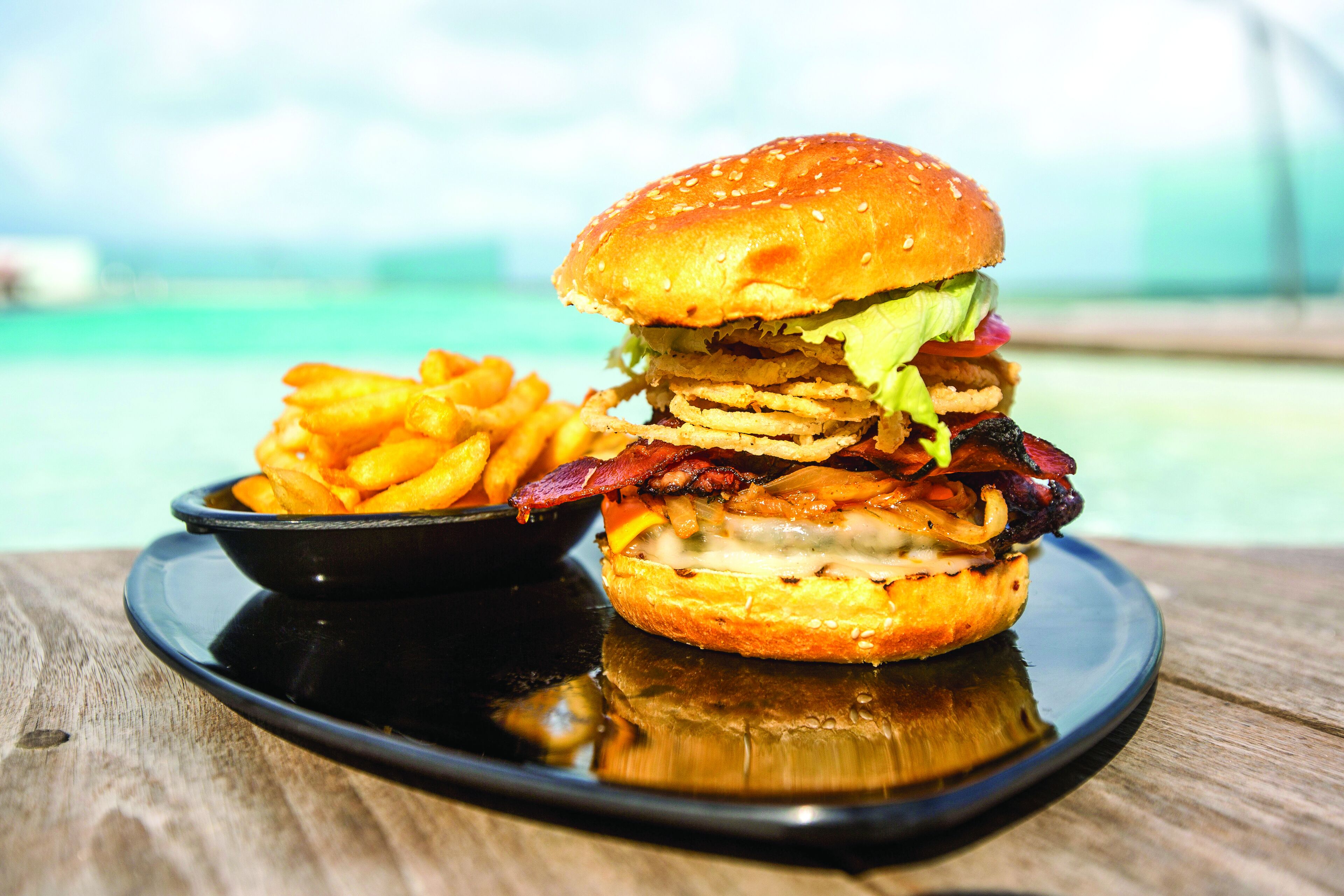 Hamburguesa y papas fritas sobre un plato negro, con una mesa de madera.