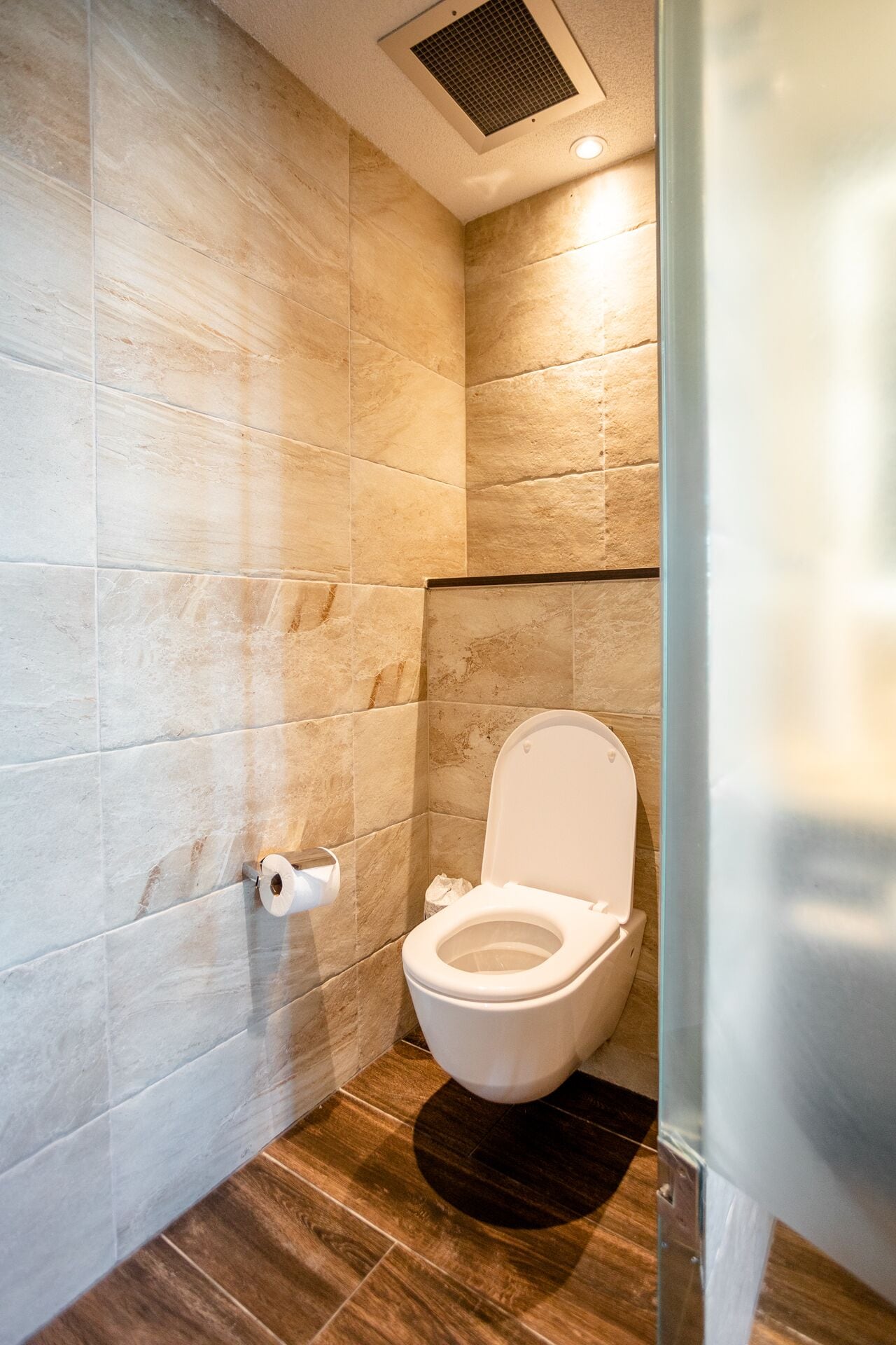 A modern bathroom with a toilet, a hand dryer, and a vent on the ceiling.