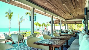Ein Sitzbereich im Freien mit Holztischen und -stühlen mit Blick auf einen Strand.