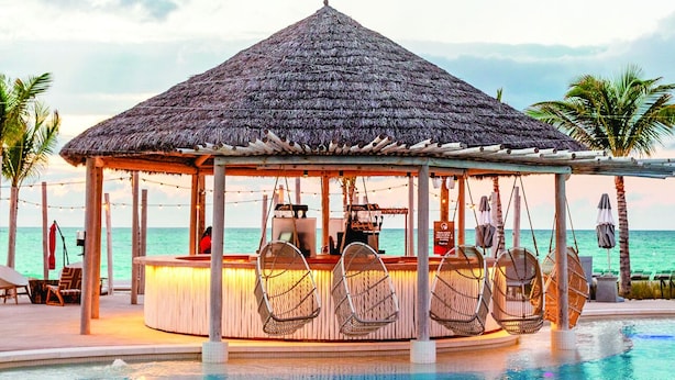 Ein Poolbereich am Strand mit einem strohgedeckten Pavillon, Liegestühlen und einer Bar.