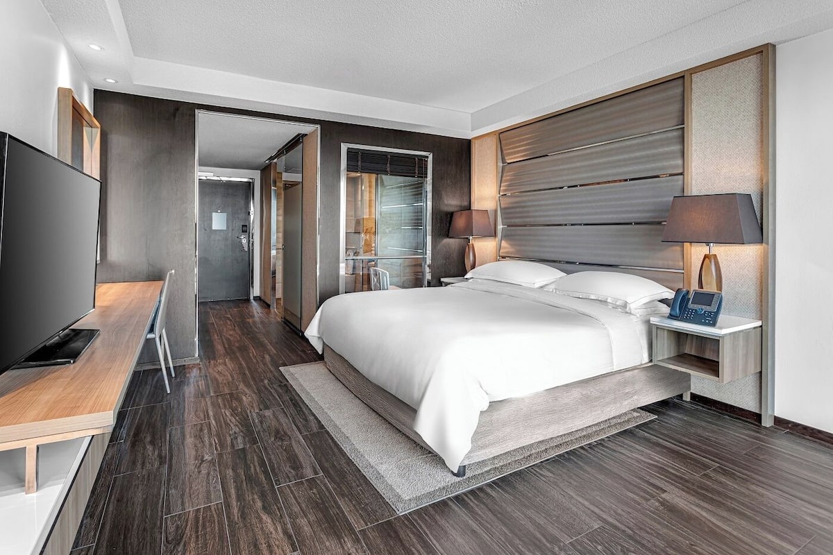 A modern hotel room with a large bed, bedside tables, a desk, and a TV.