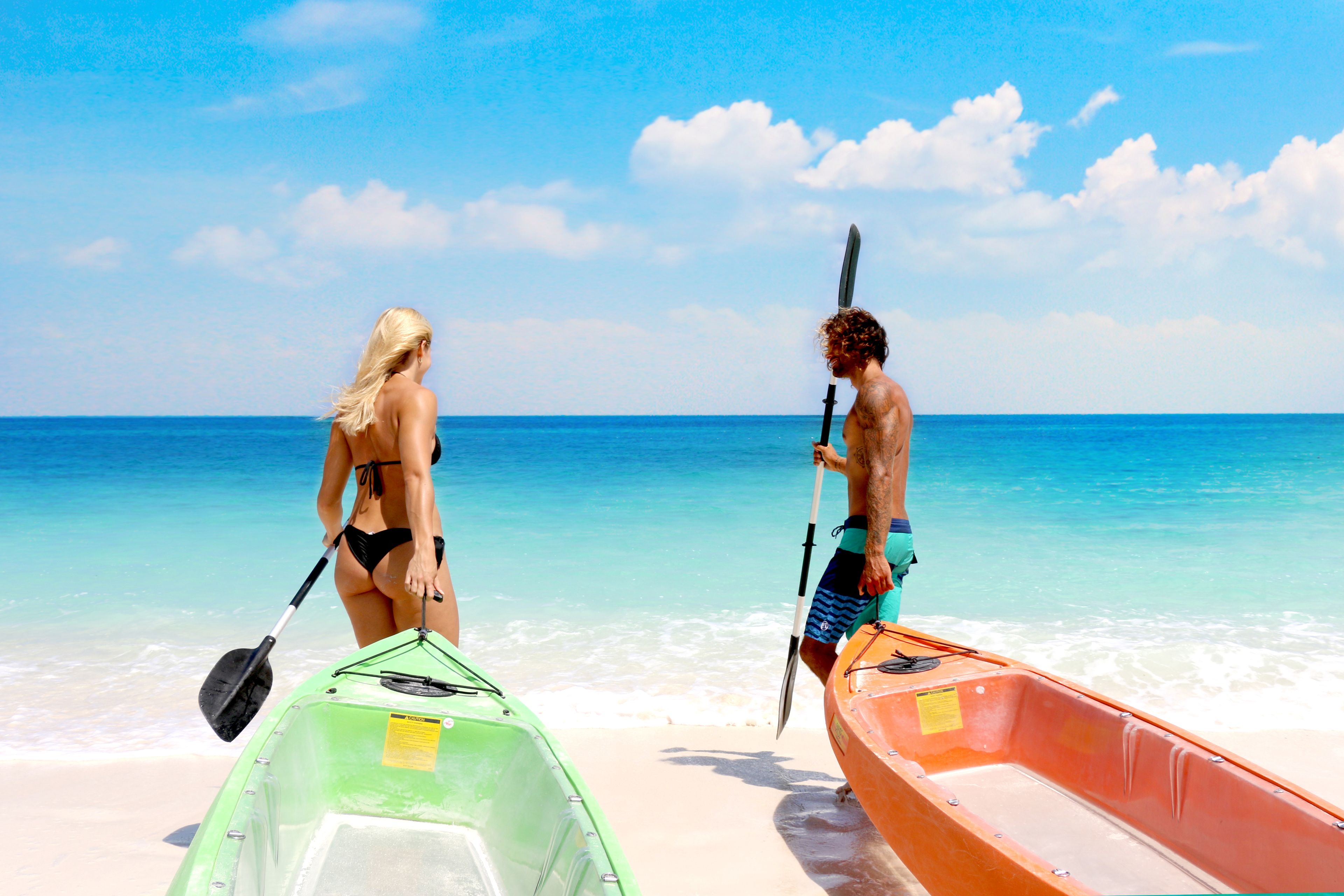 A beach scene with two kayaks and a person holding a paddle.