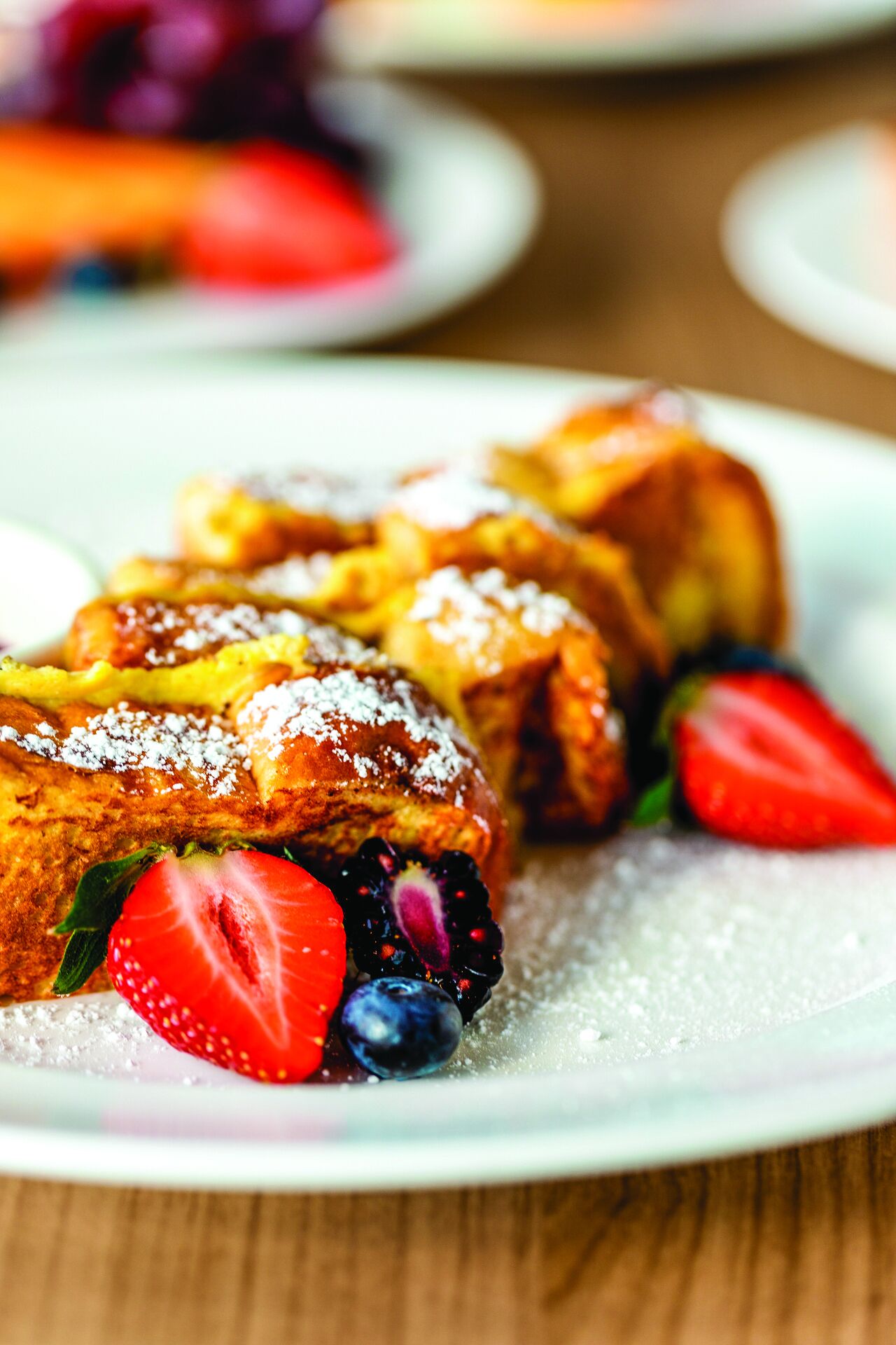 A plate of French toast with strawberries and blueberries, dusted with powdered sugar.