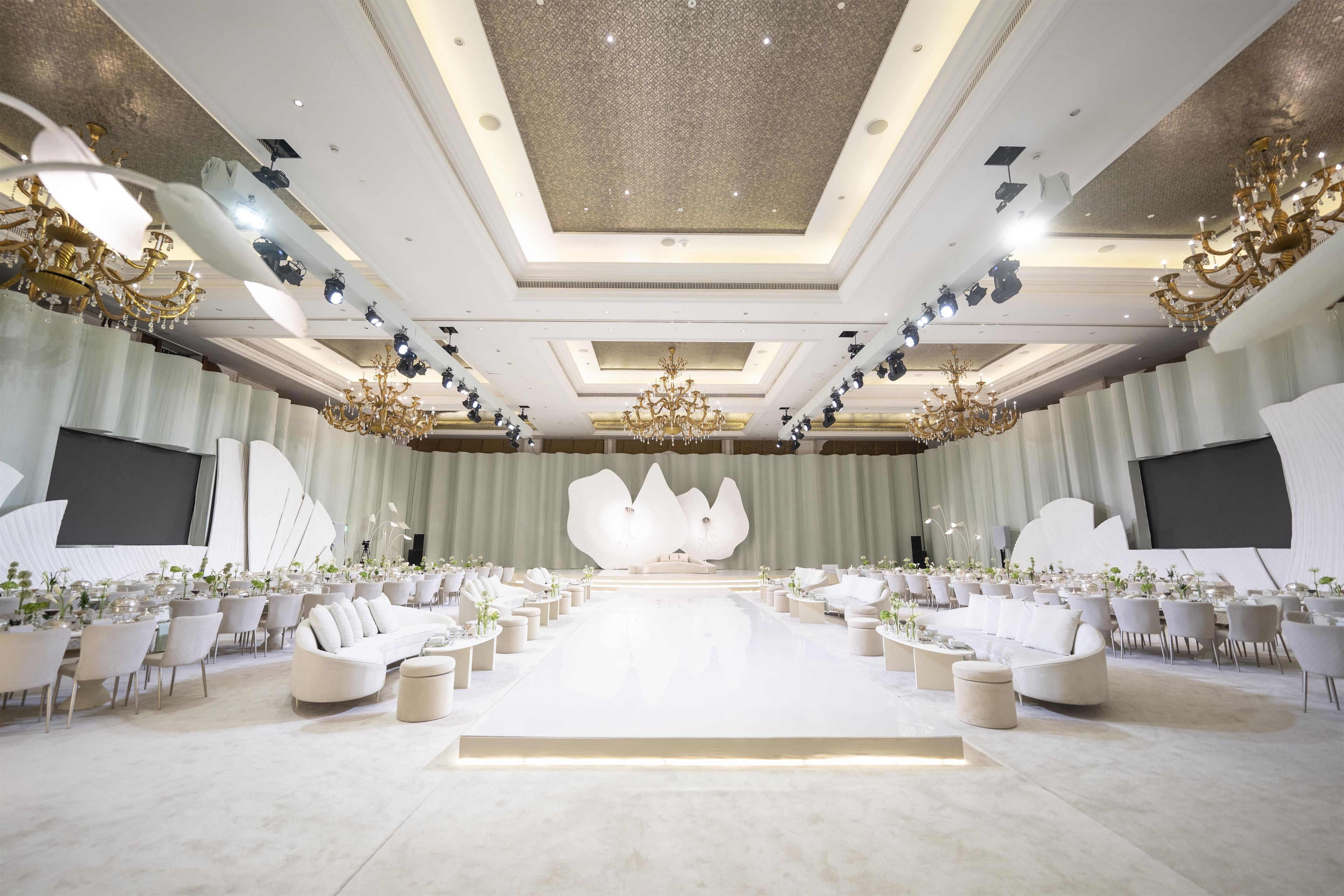 A spacious conference room with a stage, rows of chairs, and a large chandelier.