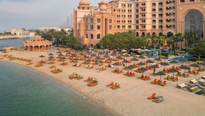 Un hotel grande con varios pisos y estructuras abovedadas, una playa con numerosas tumbonas y sombrillas, y un mar tranquilo.