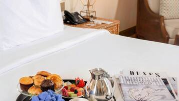 Un lit bien fait, avec un plateau de viennoiseries, une cafetière et une tasse de café posés sur une table dans une chambre d’hôtel.