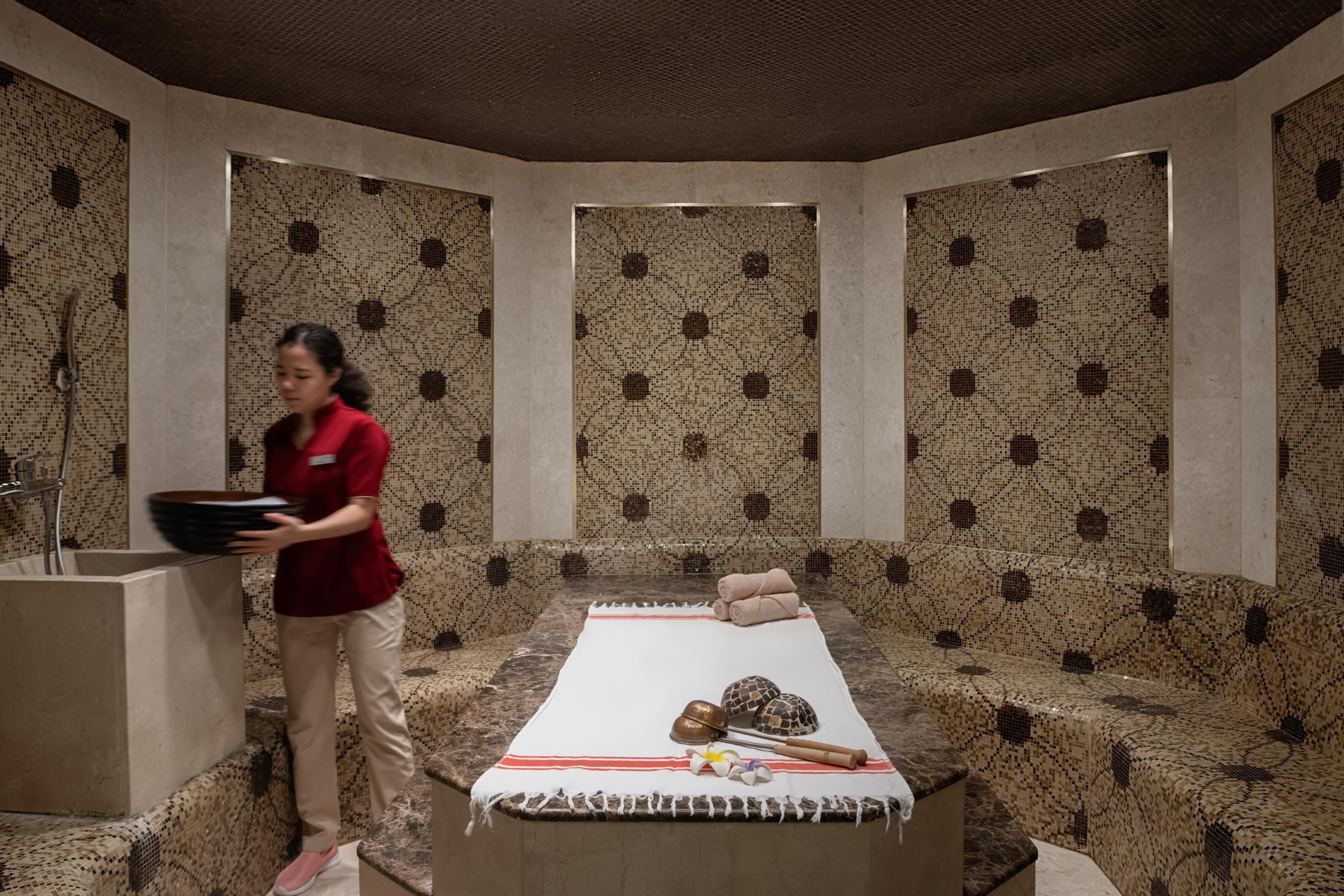 Un cuarto de spa con una camilla de masaje, toallas y una persona sosteniendo una bandeja.