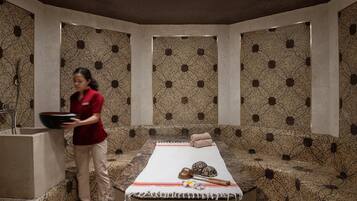 Un cuarto de spa con una camilla de masaje, toallas y una persona sosteniendo una bandeja.