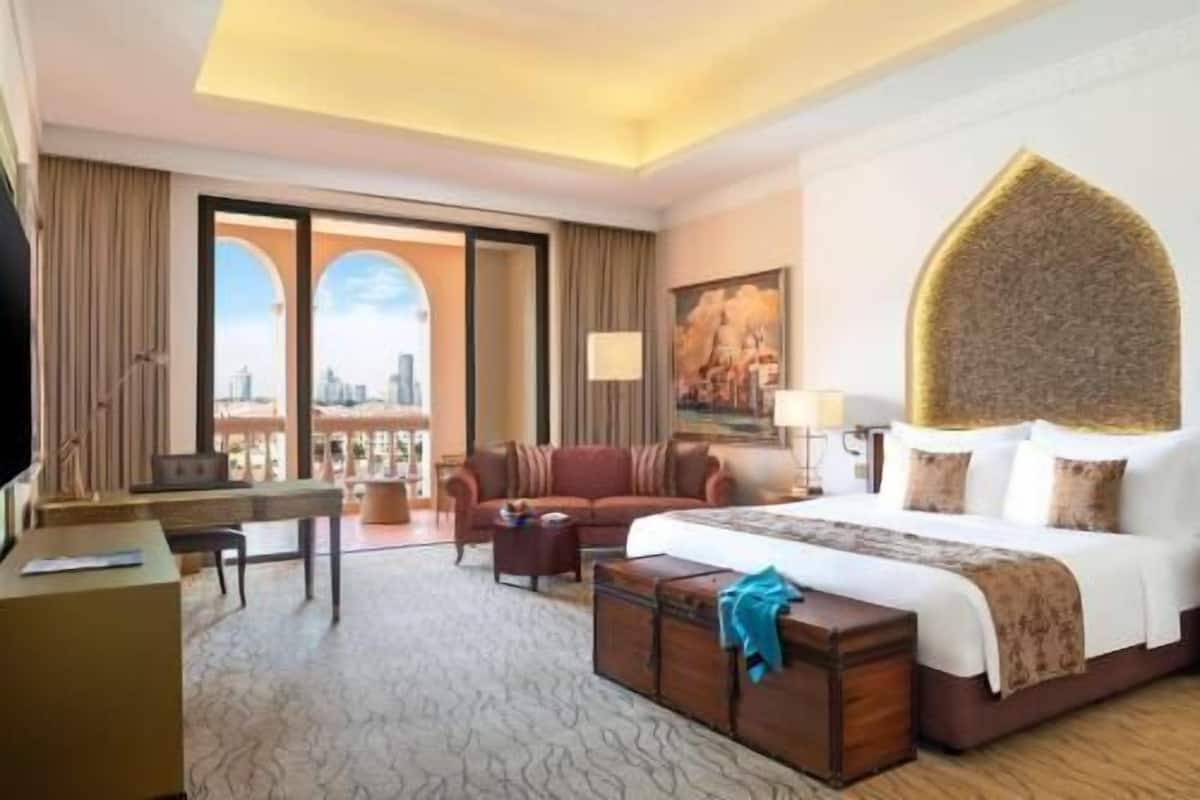 Une chambre d’hôtel avec un lit, un bureau, un canapé, une grande fenêtre donnant sur la ville et un tableau au mur.