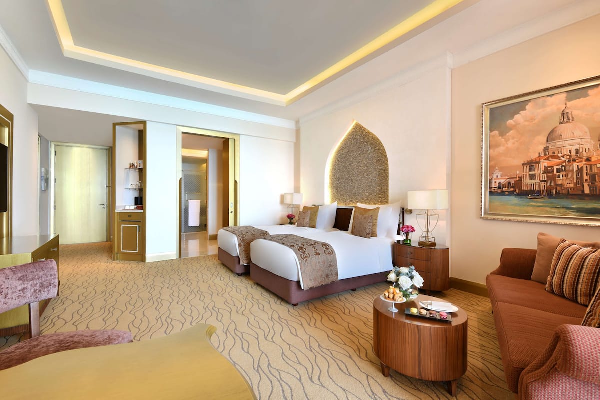 Une chambre d’hôtel avec un lit, un canapé, une table basse ronde et un tableau au mur.