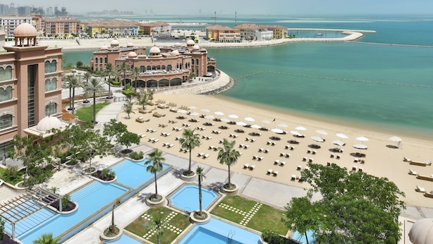 Un resort con varias piscinas, una zona de playa con tumbonas y vista al mar.