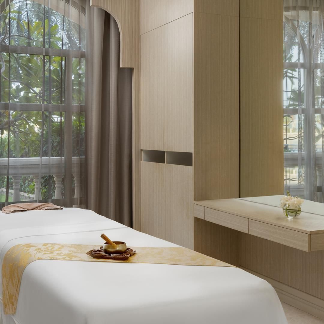 A modern hotel room with a large window, a bed with a decorative headboard, a bedside table with a vase of flowers, and a wall-mounted cabinet.